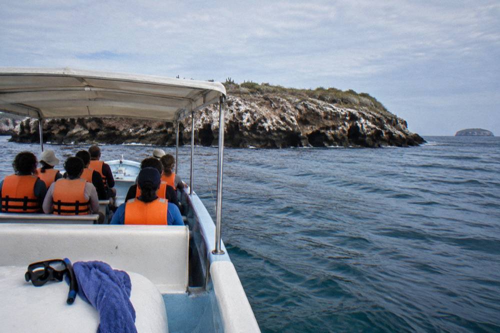 Passengers in orange life jackets riding a tour boat past a rocky island