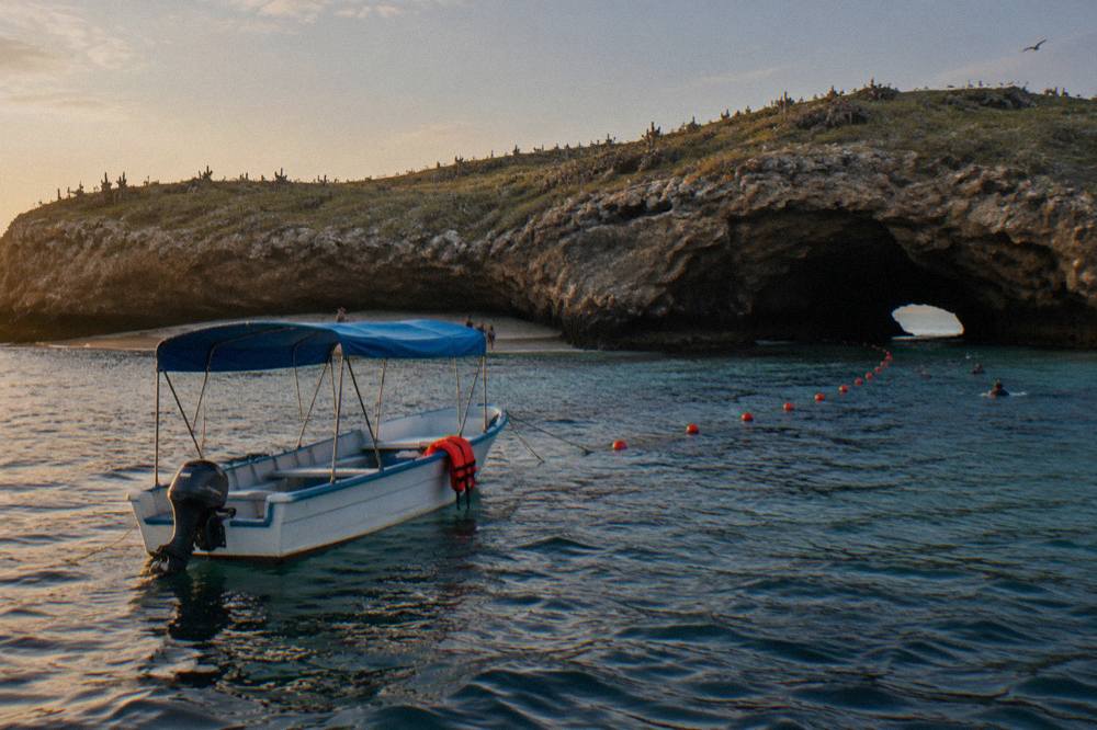 A small covered boat anchored near rocky cliffs at the Marietas Islands