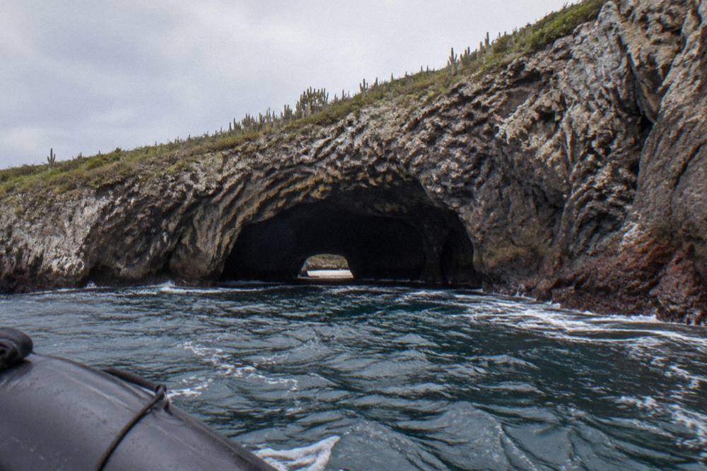 A rocky tunnel opening at sea level leading toward a hidden cove