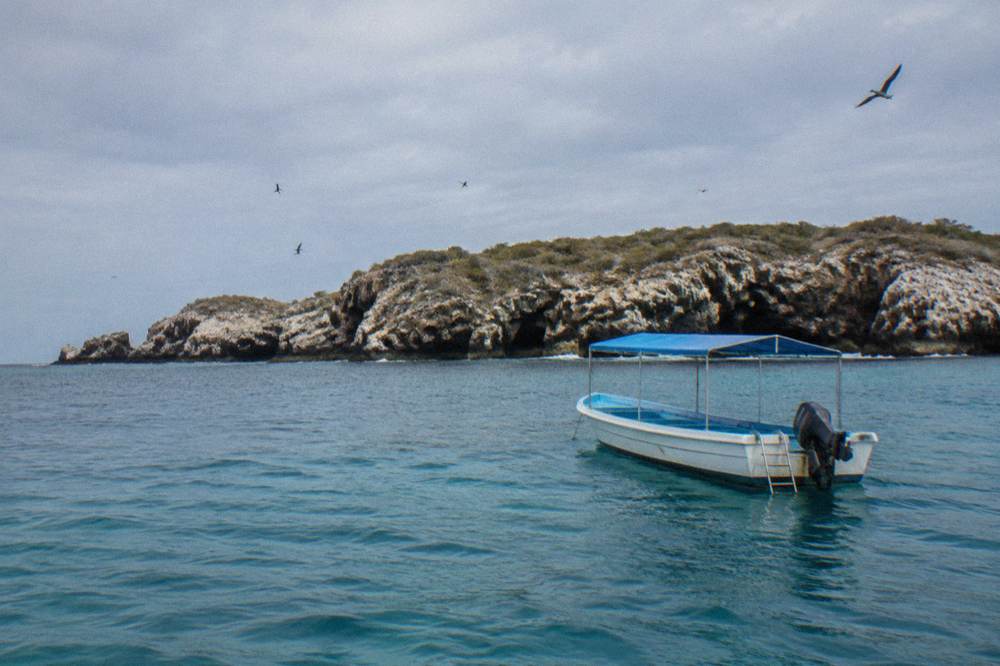 Small canopy boat floating on turquoise water near a rocky island with sea caves