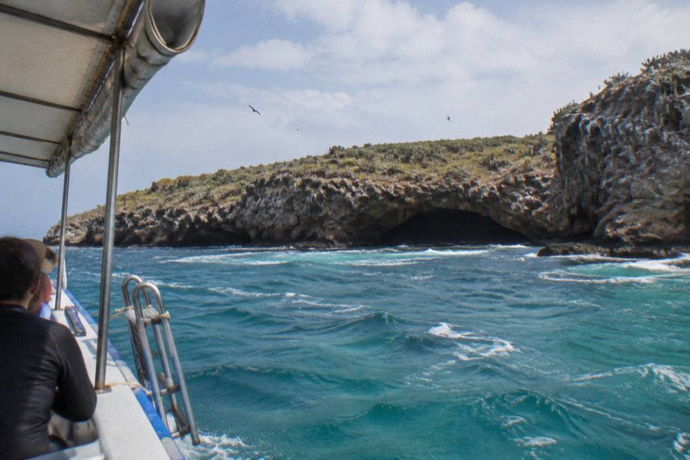 View from a boat approaching a rocky island with a dark sea cave entrance