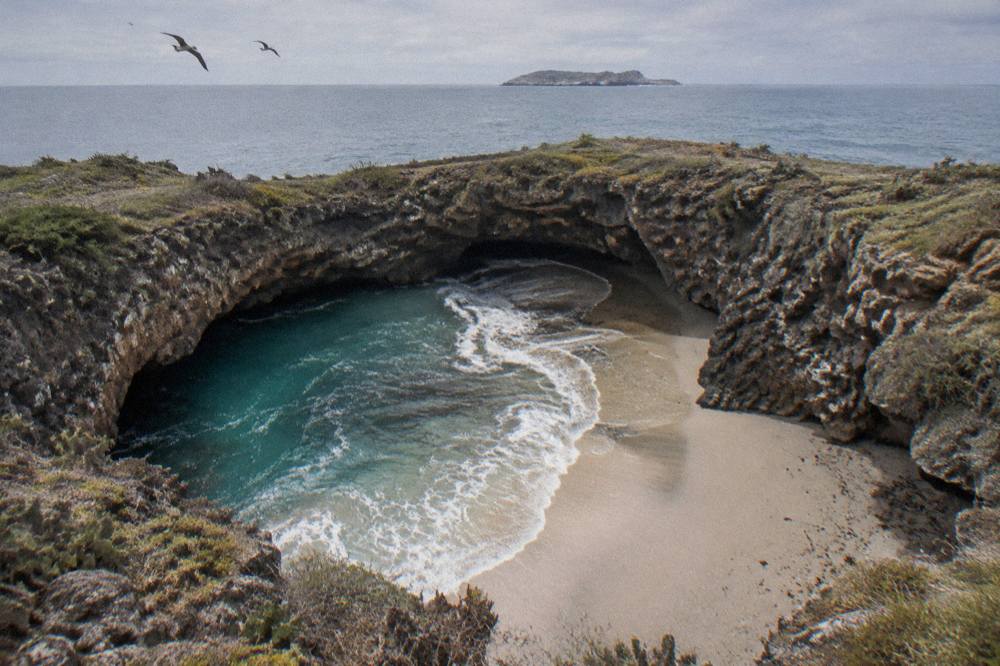 A narrow sandy beach enclosed by tall rock walls inside a crater