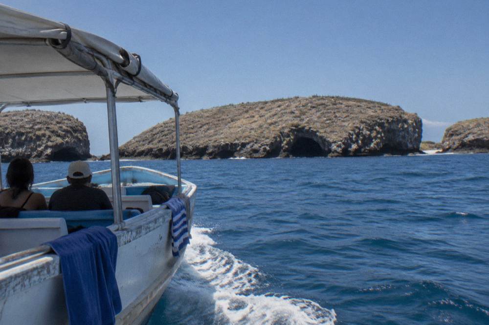 A covered small boat approaching rocky islands in open blue water