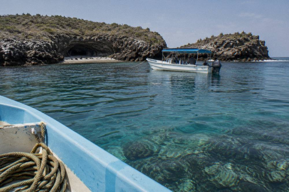 Clear turquoise water toward a rocky island cave with an anchored tour boat outside