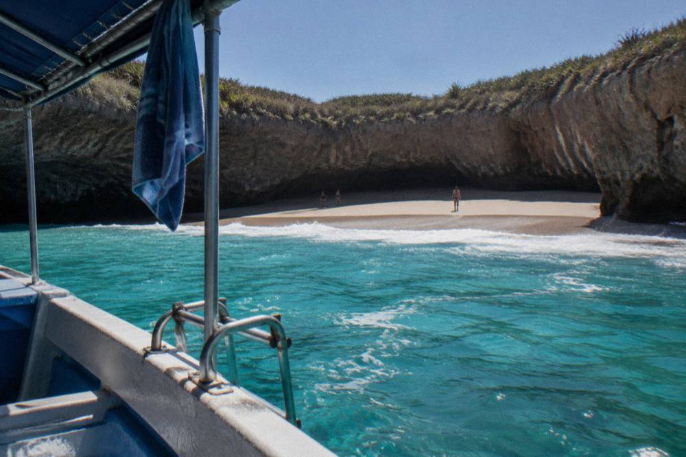 Sandy beach inside a rocky crater with turquoise water seen from a boat