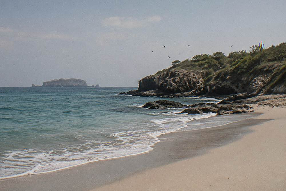 A sandy beach curving along a rocky point with gentle waves and open sky