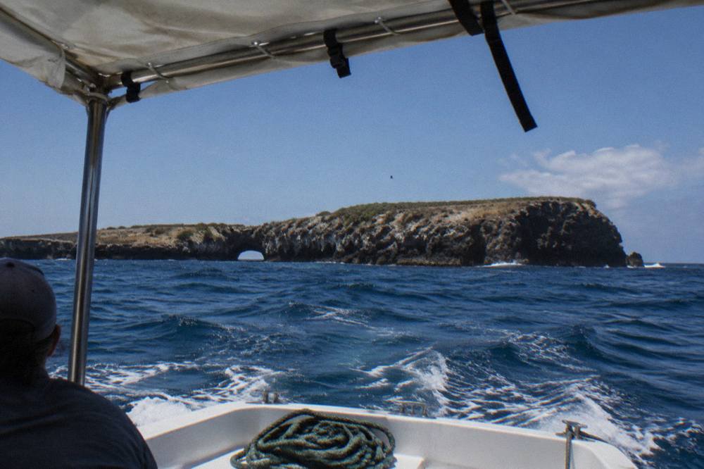 A covered small boat crossing open blue water toward rocky island cliffs