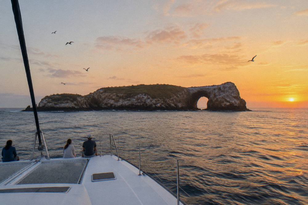 A catamaran under way on open water with guests on the forward deck