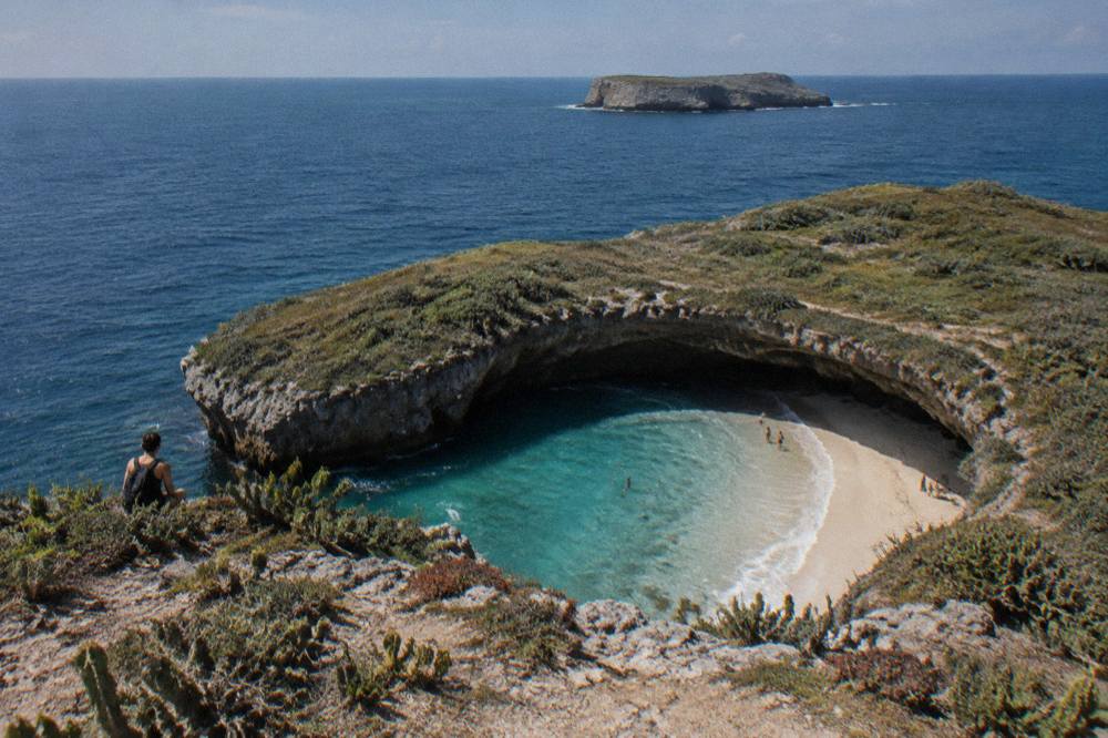 Turquoise water inside a rocky crater with a strip of sand visible below the cliff rim