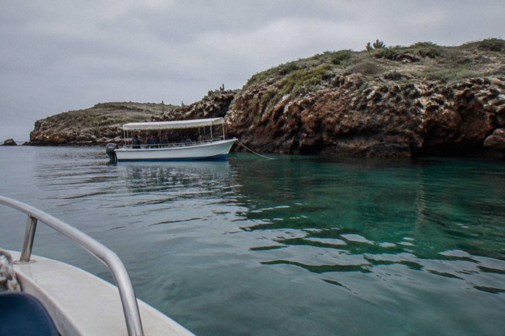 A small covered boat anchored beside rocky cliffs above clear green water