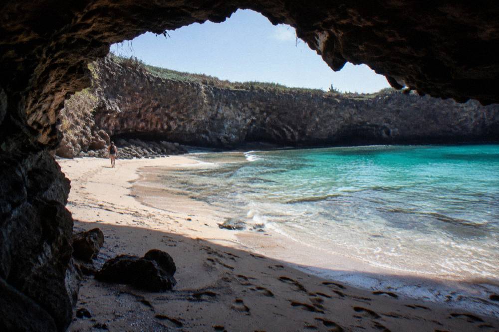 Sunlight falling through a crater opening onto sand and turquoise shallows
