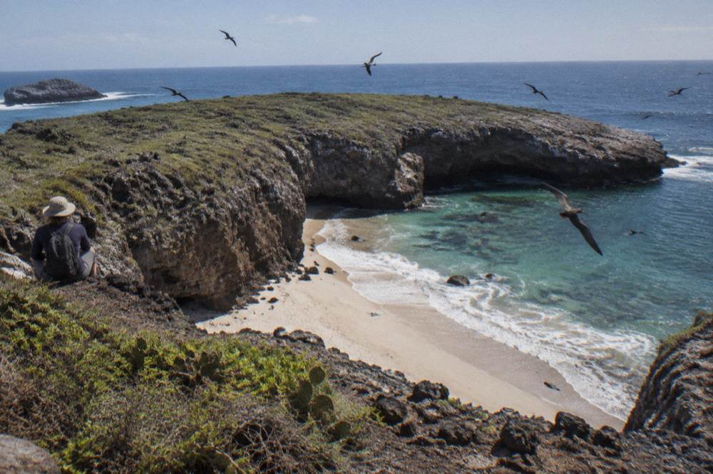 A sandy cove ringed by dark volcanic rock under an open sky