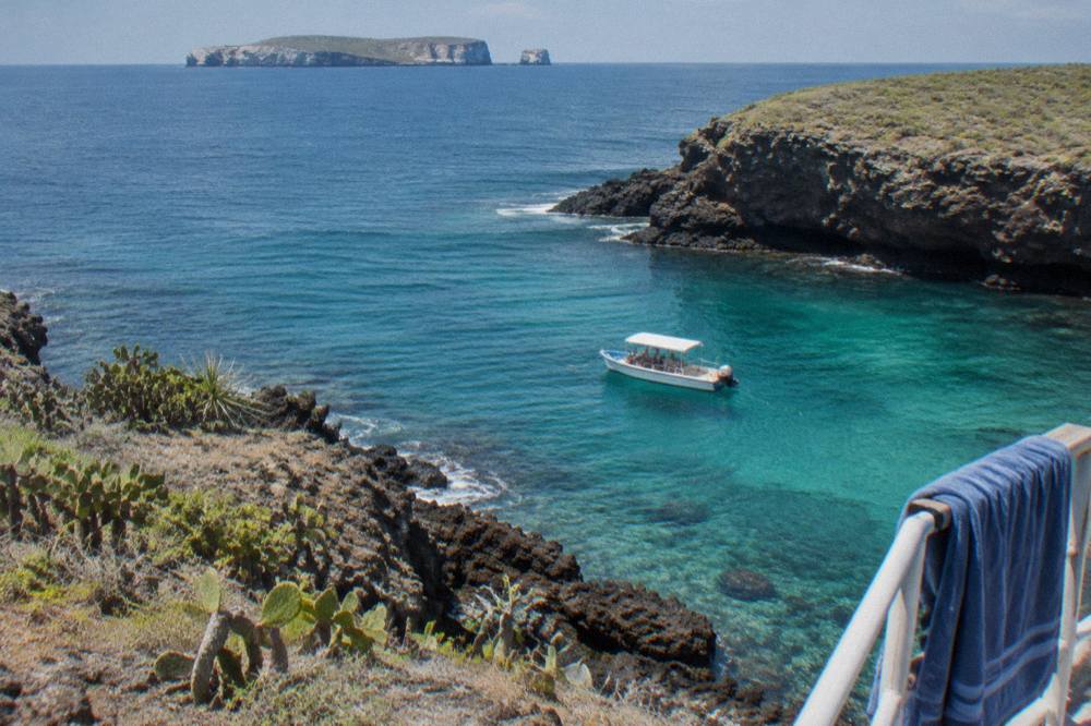 Snorkel boat anchored near rocky shoreline at the Marietas Islands in clear morning light