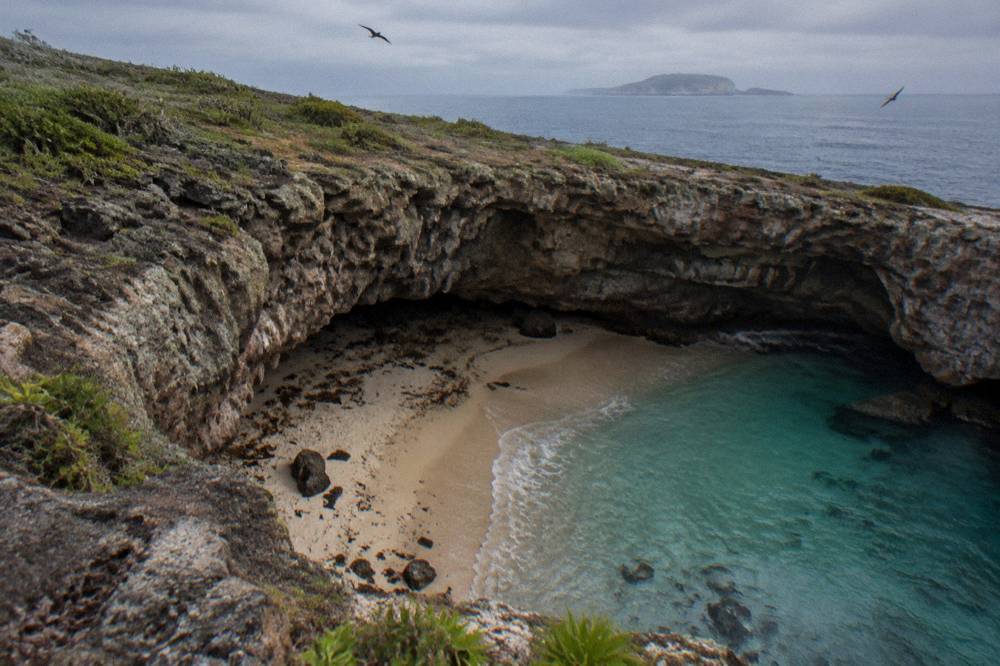 Hidden beach inside a rocky crater seen from above with turquoise water at its center