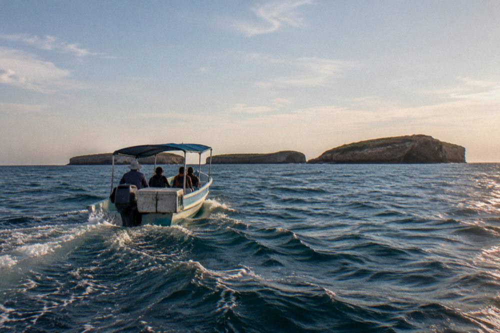 Small covered boat with passengers heading toward island cliffs on open water