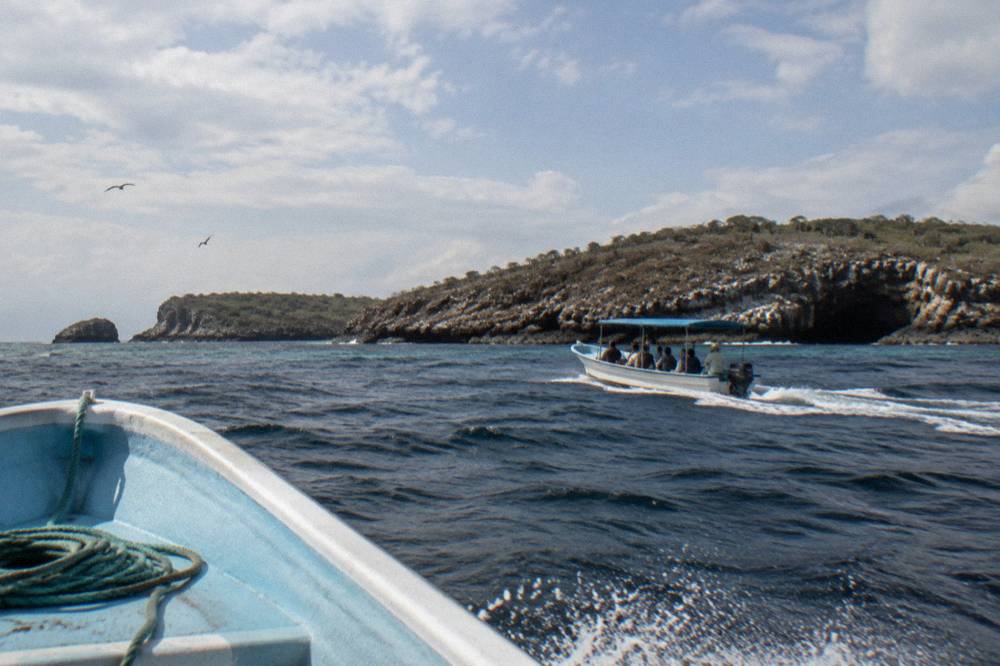 A small covered boat cruising near steep volcanic cliffs at the islands