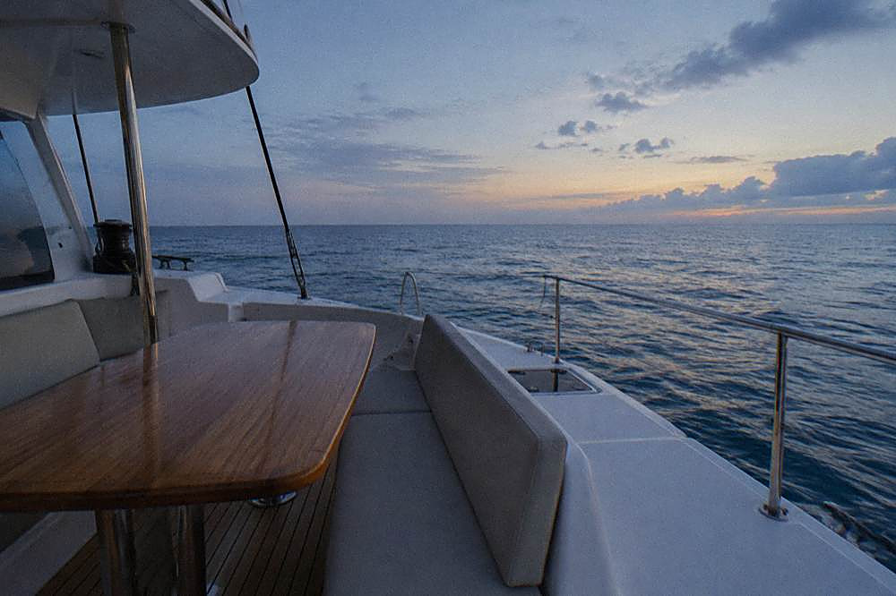 Wooden table and cushioned seating on a boat deck overlooking open ocean