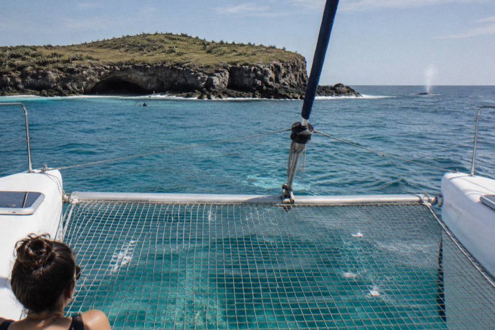 The twin hulls and net of a catamaran with turquoise water passing beneath
