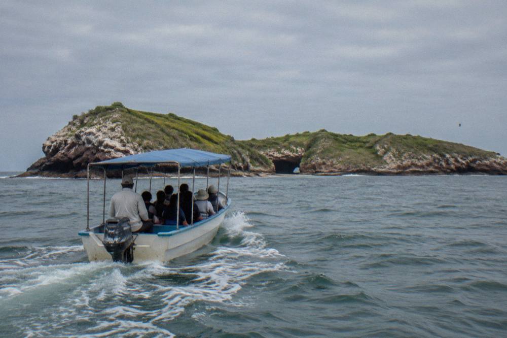 A covered small boat crossing open water under a grey sky near island cliffs