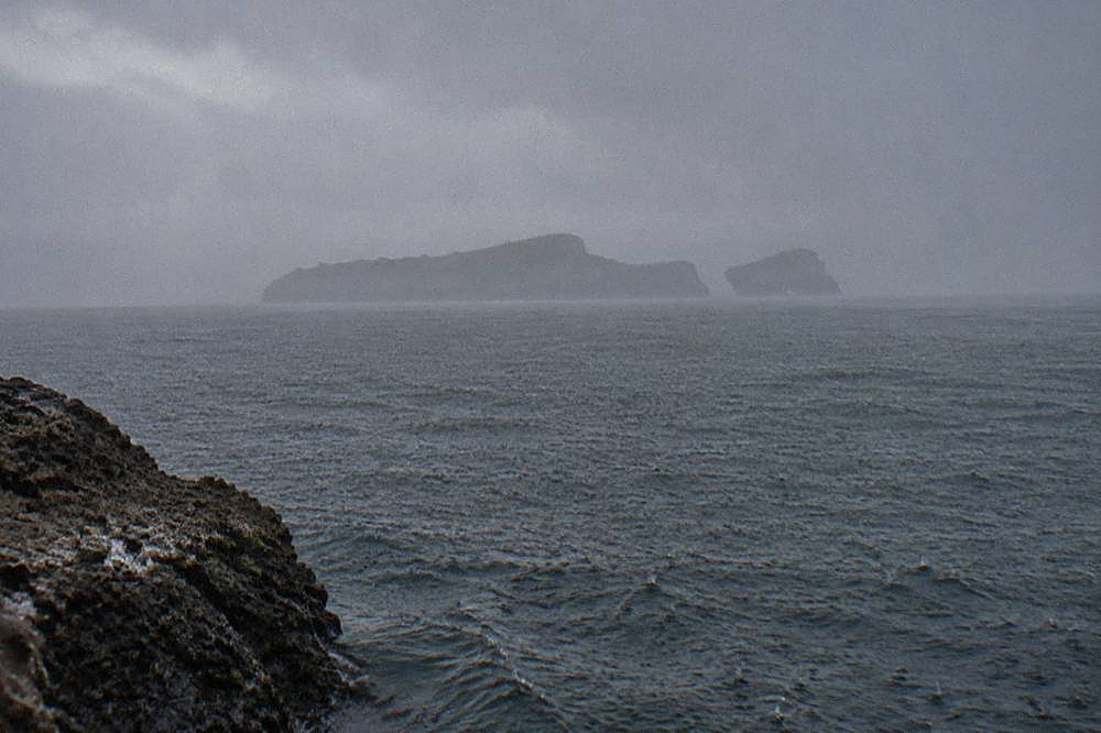 Rocky shore overlooking a choppy grey sea with misty islands on the horizon