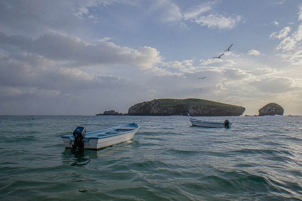 Two small motorboats on calm water near a large green island with a smaller islet