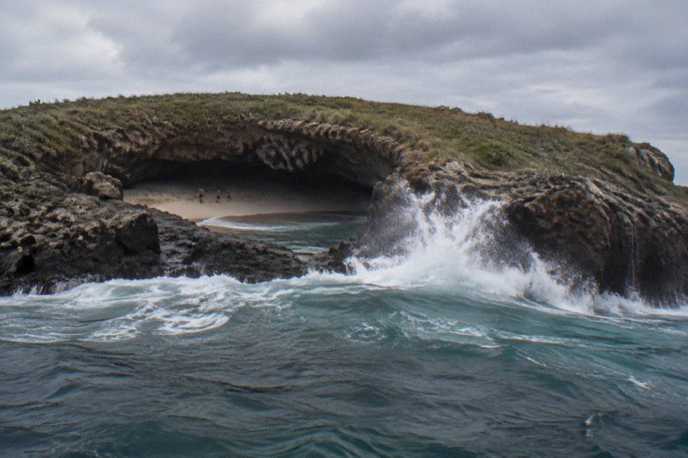 Ocean swell breaking against a rock arch and crater wall at an island shore