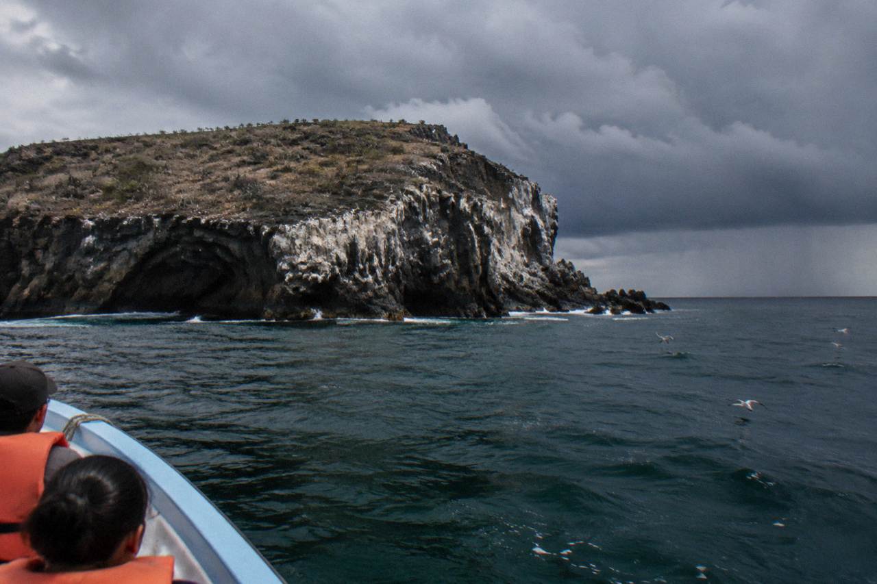 Boat passengers in orange life jackets approaching a rocky island cliff with a sea cave