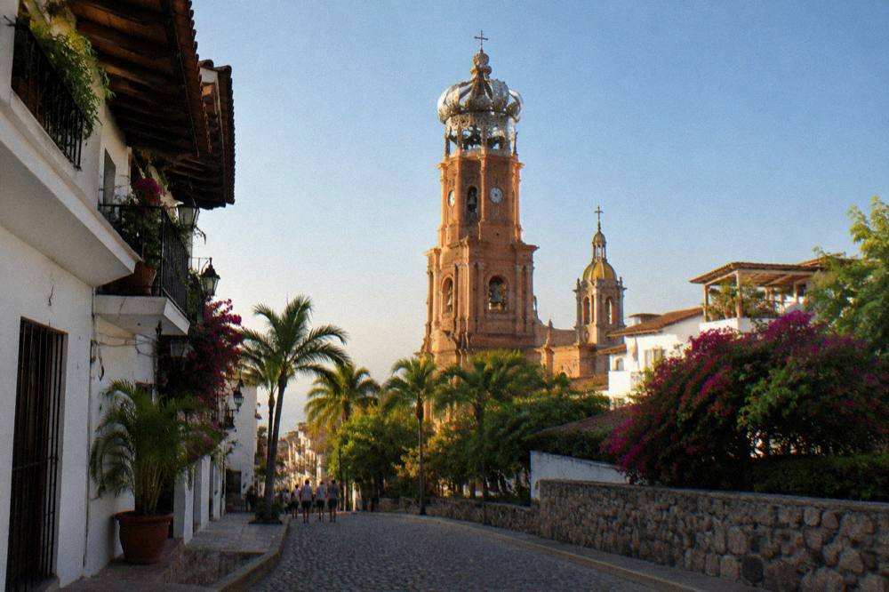 Cobblestone street with palm trees and white buildings leading to a crowned church tower
