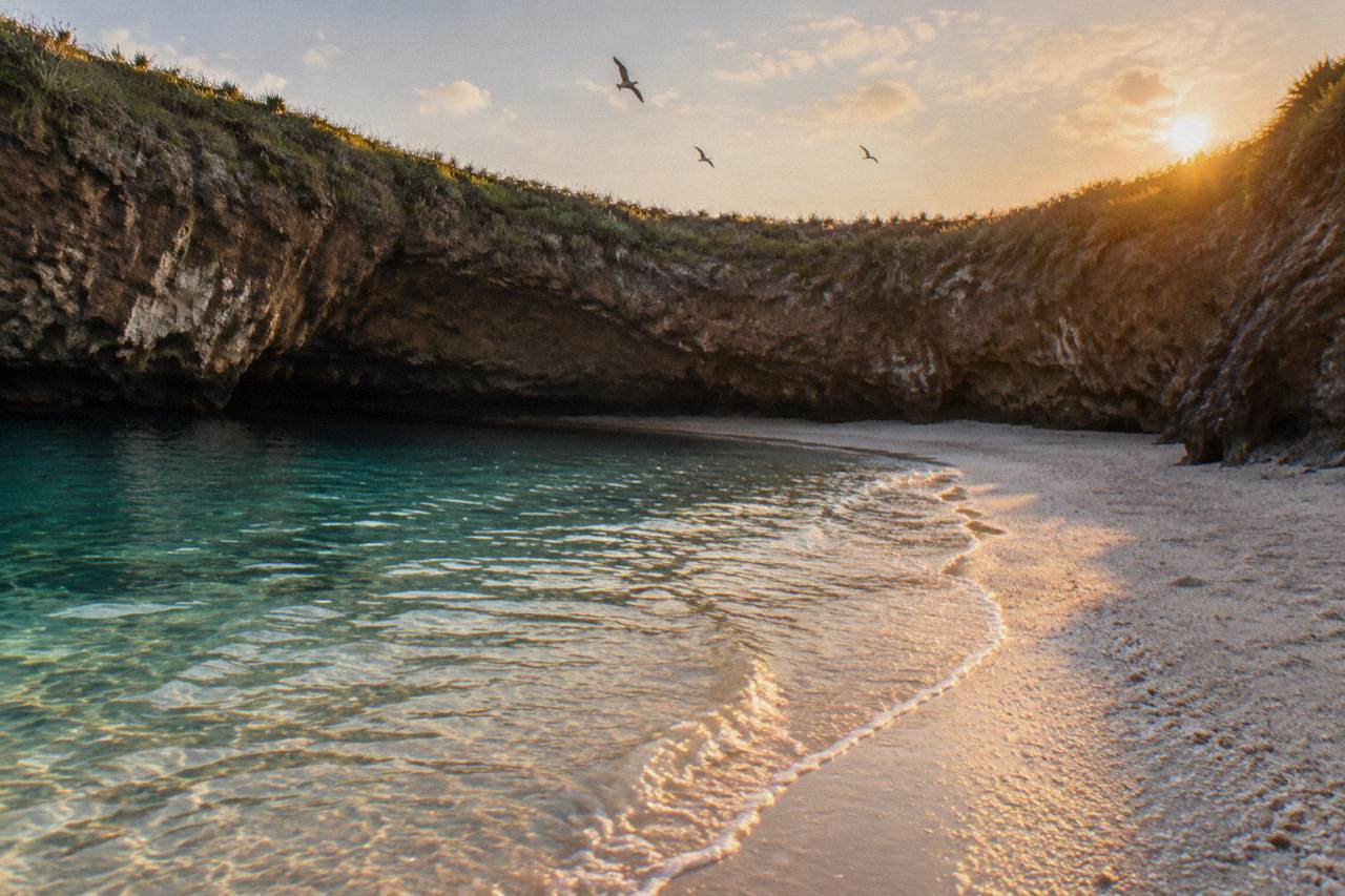 A sandy beach inside a rocky crater open to the sky, with cliffs and turquoise water