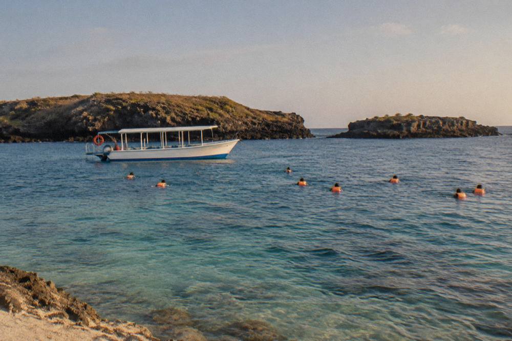 A boat anchored near tall rock cliffs at the Marietas Islands with snorkelers in the water beside the reef