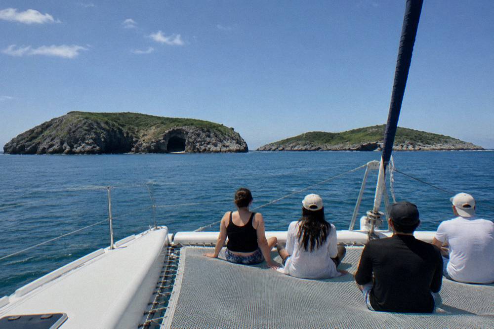 People seated on a boat deck looking toward green rocky islands with cave openings