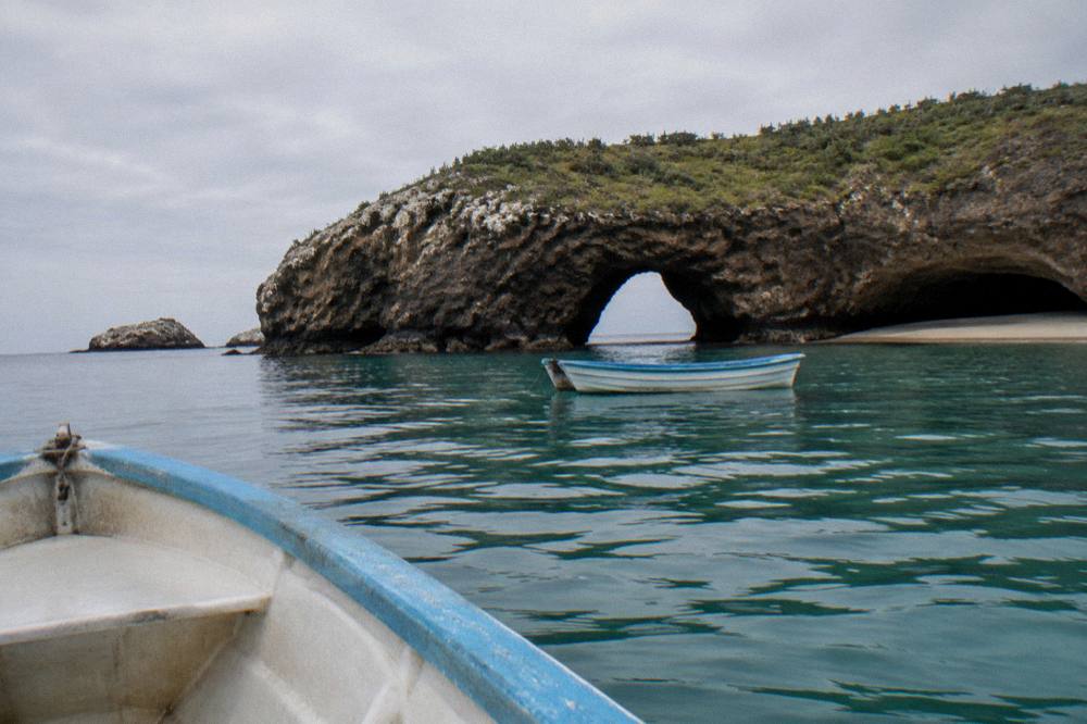An empty boat resting in shallow clear water near a rock arch formation