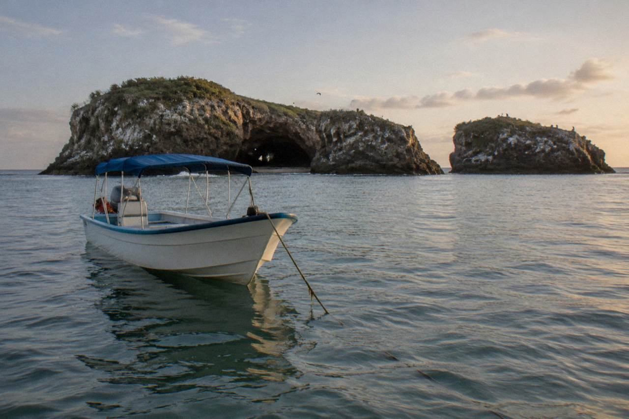 A small covered boat anchored near rocky islands in calm blue water
