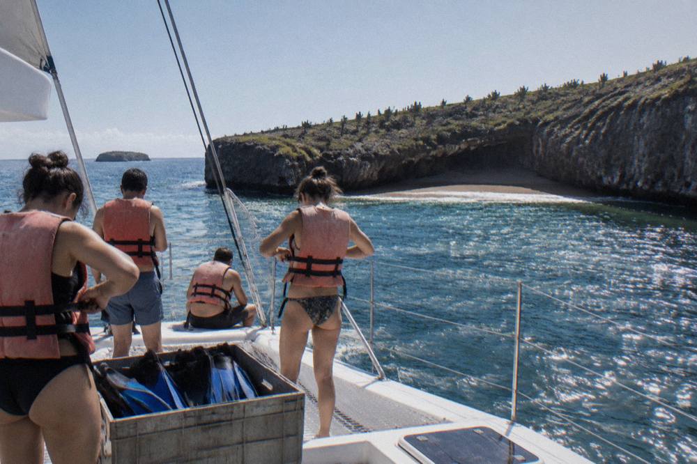 People in life jackets on a boat near a rocky crater with a sandy beach