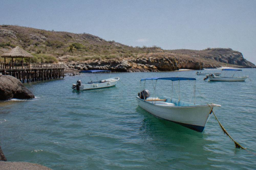 Small white boats with blue canopies anchored in a turquoise bay beside a wooden pier