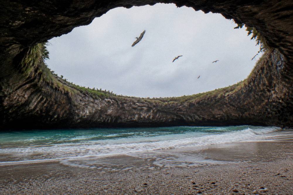 A sandy beach inside a rocky crater open to the sky above the sea