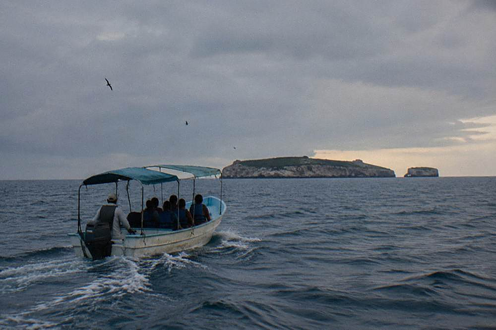 A covered tour boat with passengers in life jackets heading toward a rocky island