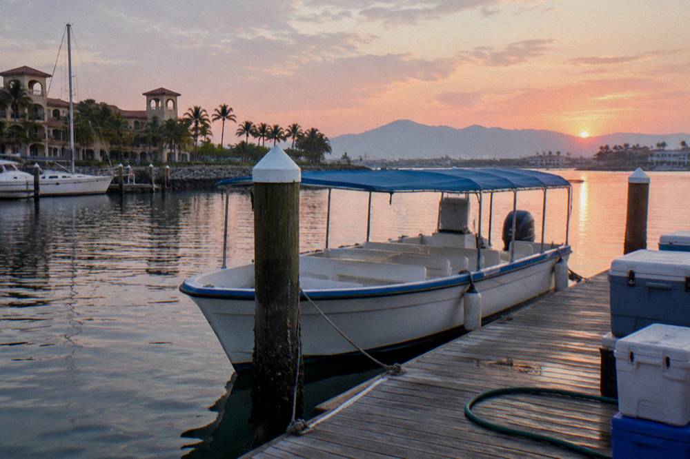 White boat with blue canopy moored at a wooden dock near resort buildings