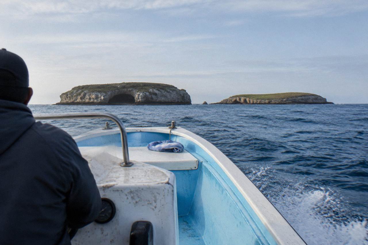 A small boat crossing open water toward rocky islands on the horizon under a wide sky