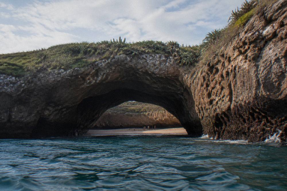 Rocky tunnel opening at sea level leading toward a crater beach
