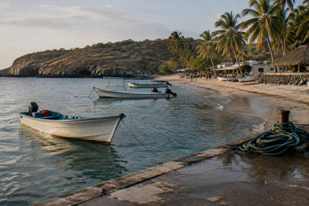 Fishing boats moored at a small pier beside a village beach