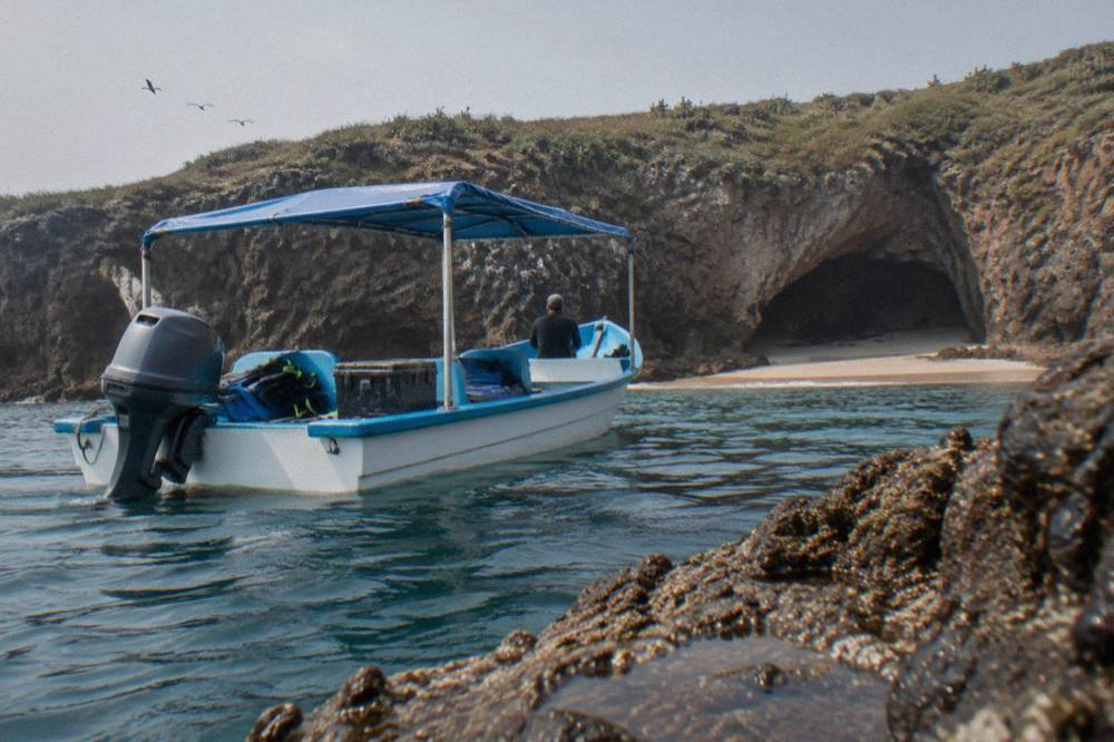 A small covered boat on calm water near a rocky cliff with a cave opening