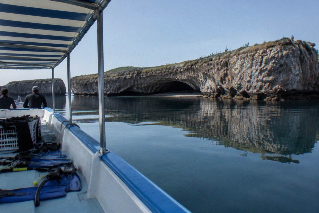 Snorkel gear on a boat deck near a rock island with a cave opening