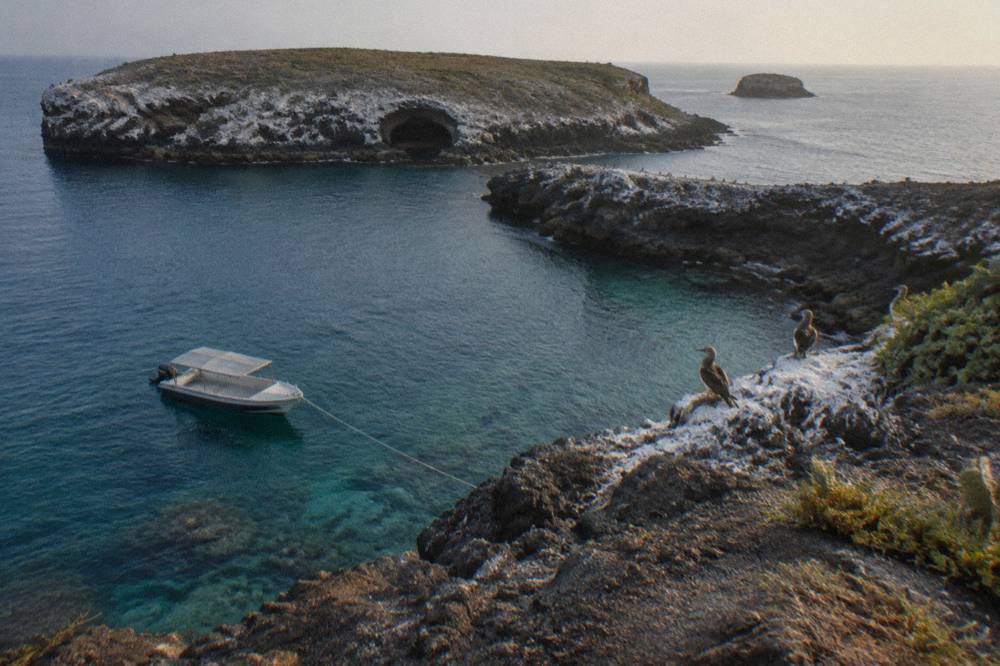 A small boat anchored beside tall rock cliffs above translucent blue water