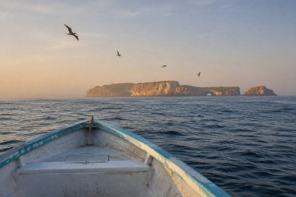 Bow of a weathered boat crossing open ocean toward distant rocky islands
