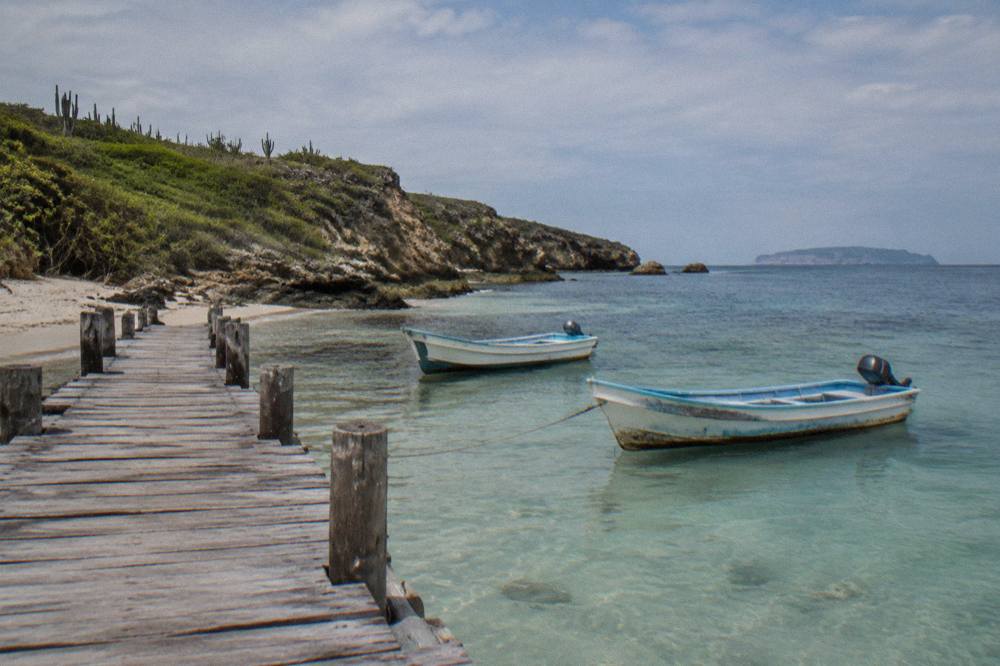 Wooden pier extending into clear turquoise water with two small motorboats nearby