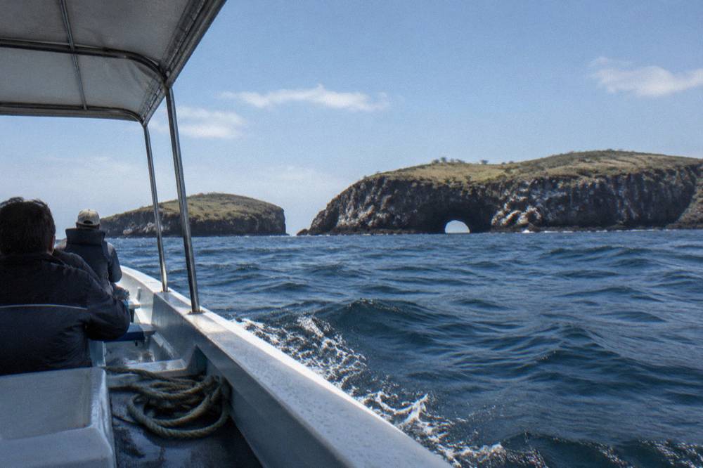 A covered panga boat heading toward rocky islands on open water