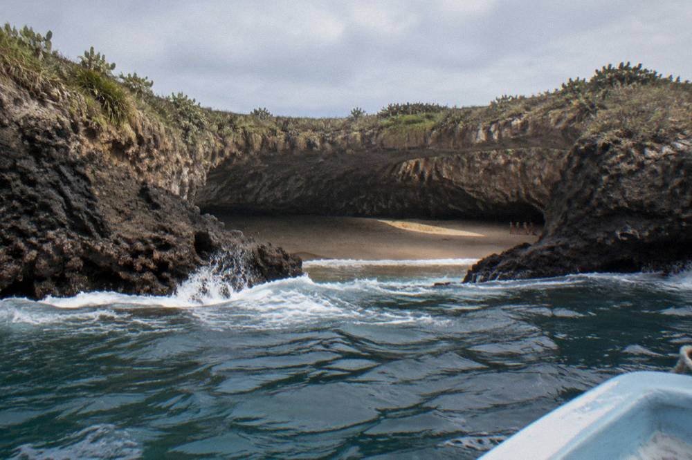 The circular crater opening of Hidden Beach seen from the water with waves at the rock rim