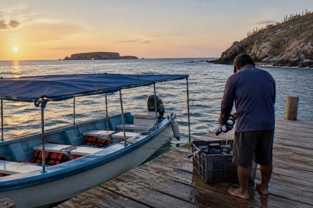 A covered panga boat at a wooden pier in Punta de Mita with crew preparing snorkel equipment