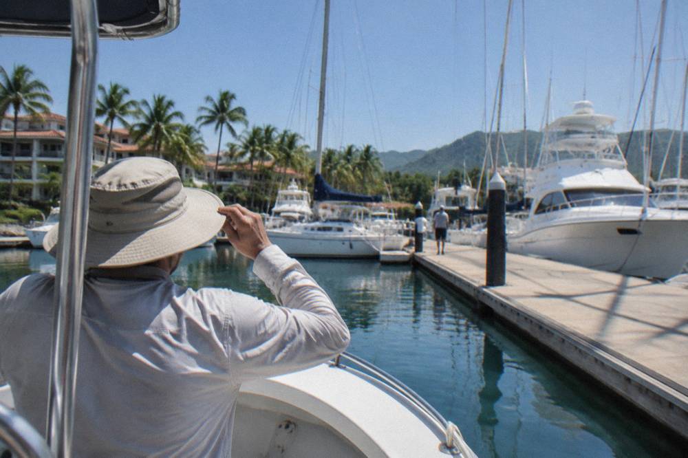 Person in a wide-brimmed hat on a boat in a marina with yachts and palms